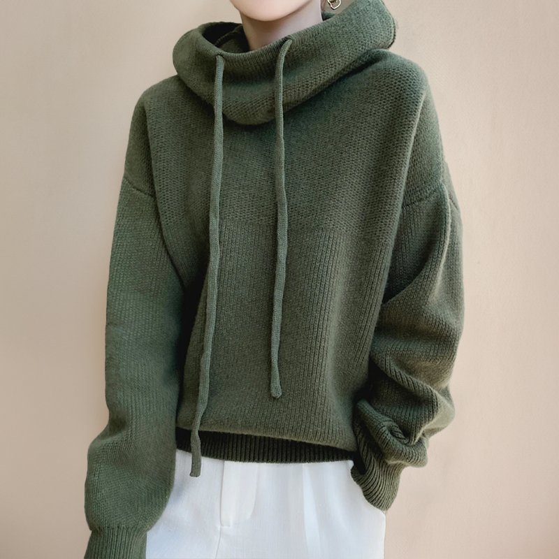 Dark olive green knitted jumper with long drawstrings at the roll neck, worn with white trousers 2