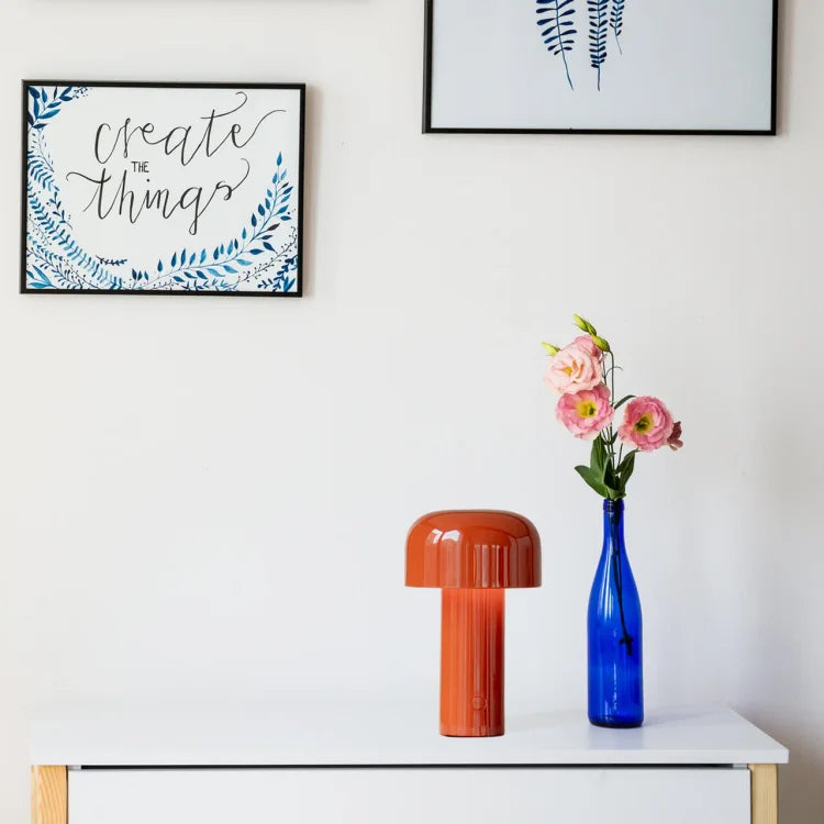 Orange mushroom lamp on a white sideboard beside a blue bottle holding pink flowers 20