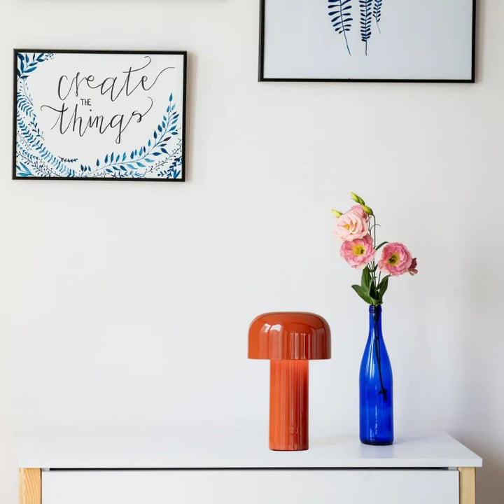 Orange mushroom lamp on a white sideboard beside a blue bottle holding pink flowers 20