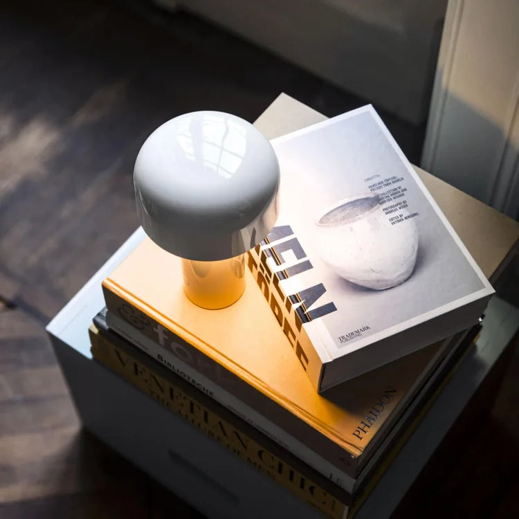 White glossy mushroom lamp glowing warmly on a stack of hardback books, seen from above 21