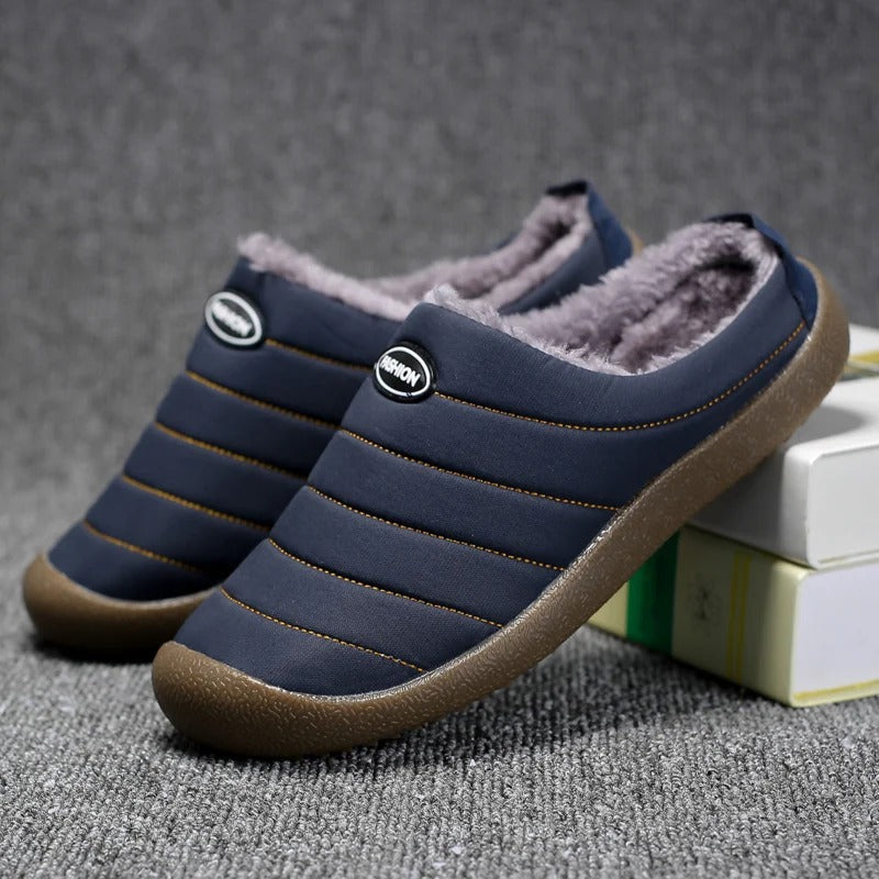 Pair of navy blue quilted slippers with fleece lining, one propped against books on grey carpet 5