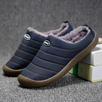Pair of navy blue quilted slippers with fleece lining, one propped against books on grey carpet 5