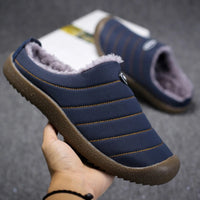 Hand holding a navy blue slipper, showing fleece lining, orange stitching and textured brown sole 6