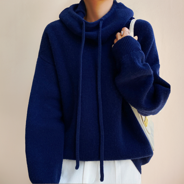 Navy blue knitted jumper with drawstring roll neck, worn over white trousers with a cream shoulder bag 8