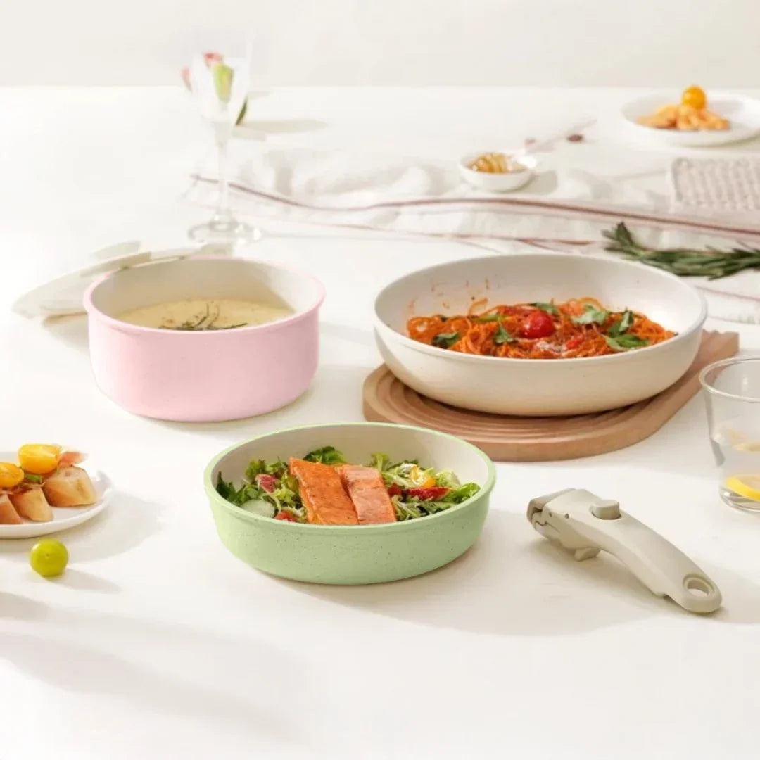 Pastel pink, green and cream pans holding soup, pasta and salmon salad on a set table, detachable handle beside them 2